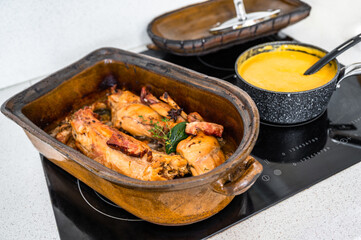 Baked rabbit rustic earthenware pan, pot with vegetable sauce and lid on ceramic hob.