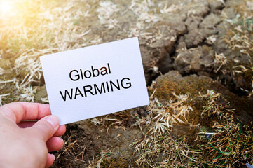 Global warming text written on white paper note in female hand over cracked soil. Climate changes concept, save planet