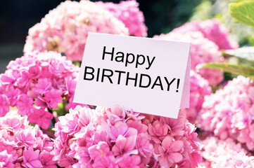 Happy birthday text written on white card with pink blooming hydrange flower, greeting card