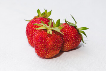 Red berry juicy strawberry. Three ripe strawberries with strawberry leaf, isolated on a white fabric background.