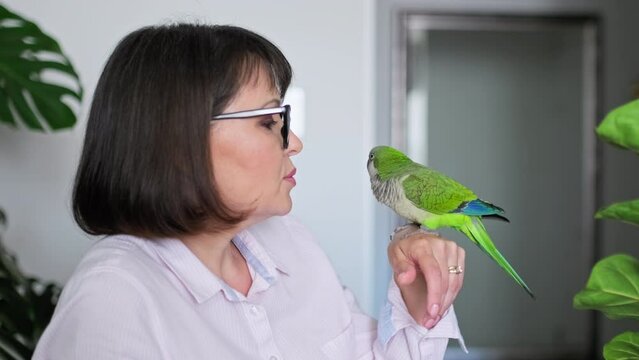 Mature woman at home with a pet parrot on her arm