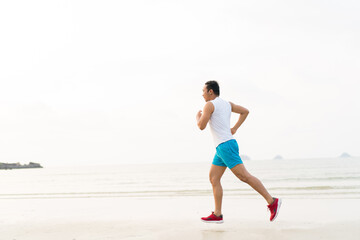 Fototapeta premium asian sport man running along seaside. running on beach with healthy toned legs body, Hamstring muscles, knee joint health active lifestyle panoramic banner background. the beach runners working out
