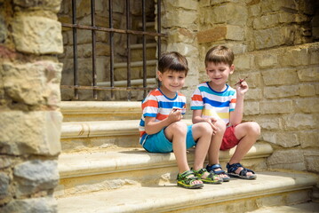 The children playing on the ruins of ancient building with metal gate an archaeological site of an ancient city. Two boys sitting and play with toy aircraft plane. Travel concept