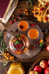 Autumn tea with berries and honey. Sea buckthorn and raspberries in a glass teapot, cups with poured tea. Apples and waffles with honey.
