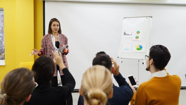 Business woman coach trainer presents a report, shows diagrams on flip chart in conference hall. Project manager reporing on presentation to employees in office. Female teacher leading a master class.