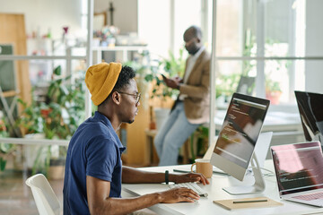 African young programmer concentrating on writing codes on new software while sitting at his workplace at office
