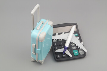 Travel budget and airplane tickets price concept. Airplane on calculator and suitcase on gray...
