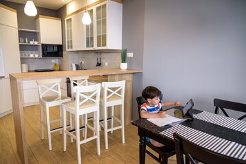 Smart preteen schoolboy doing his homework with digital tablet at home. Child using gadgets on his kitchen to study. Modern education and learning for kids