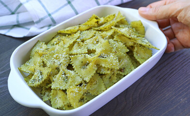 Hand Placing a Bowl of Delectable Homemade Farfalle Pasta with Pesto Sauce on Wooden Table