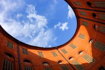 Oval roof of a round building as a commercial real estate and property management concept background with view of blue sky above an old orange house courtyard