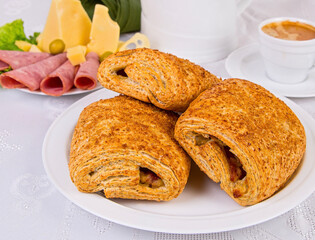 puff pastries stuffed with sausage and cheese, on a white dish, with a cup of coffee, on a white background