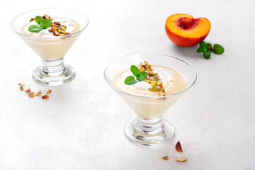 Yogurt dessert with nectarine topped with pistachio and mint in glass bowl on white table