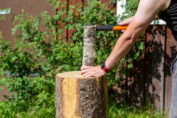 Caucasian man cutting wood outdoors with an axe. Logs piled for cold winter and warming the house with firewood in the fireplace.