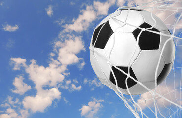 Fototapeta na wymiar Soccer ball in net against blue sky