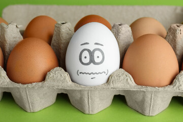 Egg with drawn frightened face among others in cardboard package, closeup