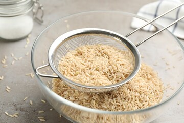 Sieve rice in bowl on grey table, closeup