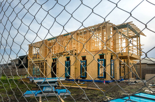 The structure of a two-story residential suburban house under construction behind fence. Concept of real estate development, self-build a new home, Australian housing market, and homeownership.