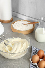 Whipping white cream in glass bowl with mixer on light grey table