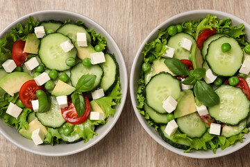 Tasty fresh salad with cucumber in bowls on wooden table, flat lay