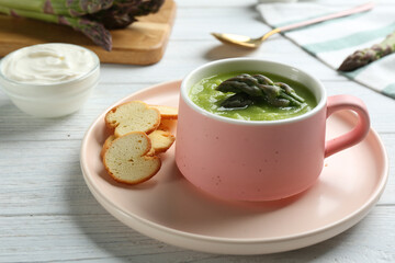 Delicious asparagus soup served on white wooden table