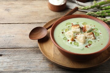 Delicious asparagus soup with croutons served on wooden table, space for text
