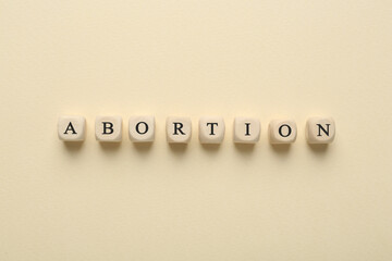 Word Abortion made of wooden cubes on beige background, flat lay