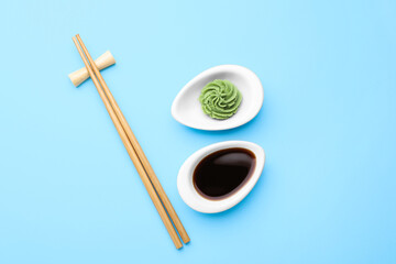 Swirl of wasabi paste, soy sauce and chopsticks on light blue background, flat lay