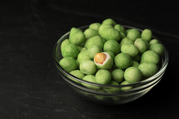 Tasty wasabi coated peanuts in glass bowl on black table, closeup. Space for text