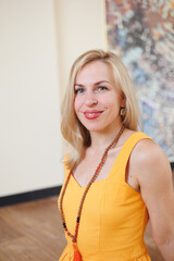 Young pretty yoga girl portrait with beads, happy and smiling. Beautiful blond woman playing with her beads in yoga pose. Woman in yellow dress indoors.