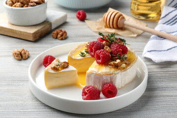 Brie cheese served with raspberries, walnuts and honey on white wooden table