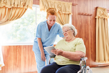 Elderly woman in wheelchair using tablet computer in nursing home