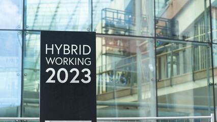 Hybrid working 2023 on a city-center sign in front of a modern office building	
