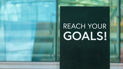 Obraz premium Reach your goals on a sign outside a modern glass office building 