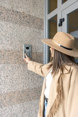 A woman wearing a hat pushing the button of the intercom of building