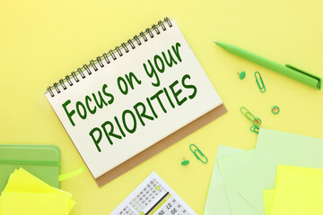 yellow background calendar green paper clips. green notepad. business concept, flat lay. text on notepad, focus on your priorities