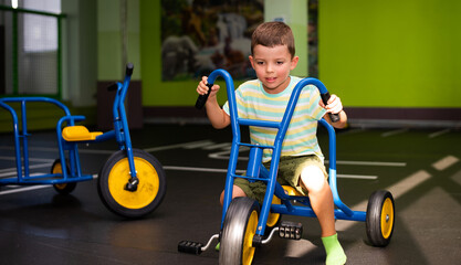 A six-year-old child boy rides a blue tricycle on a special area with markings on the road