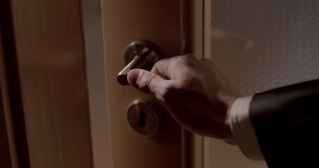 Man hand secretly opens doors knob handle, closeup. Espial is spy work. Covert surveillance in dark indoor. A gap in the door for eavesdropping and peeping. Dark, noisy.