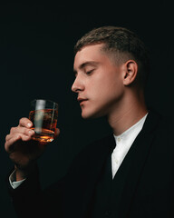 Tasting, tasting. A man in a suit holds a glass of brandy. Tasting and wine tasting concept. Young businessman in an elegant suit with a glass of whiskey. Sommelier tastes an expensive drink.