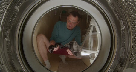 A man throws laundry into the washing machine. He throws objects into the drum of the washing machine. Closes the glass hatch with his hand. CZ, Kladno, Polska, 25.5.22