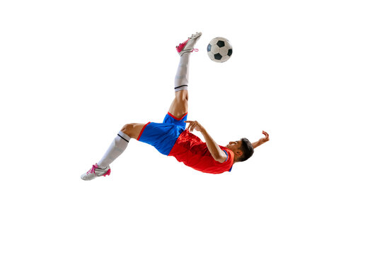 Dynamic portrait of young male football player training, kicking ball in a jump isolated over white studio background.