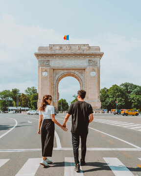 Young traveling couple holding hands near Triumphal arch