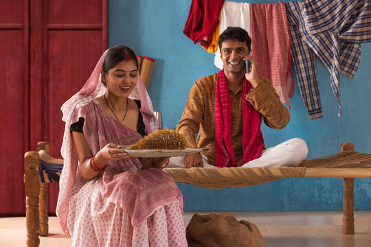 Woman cleaning paddy seeds at home while her husband talking on mobile phone