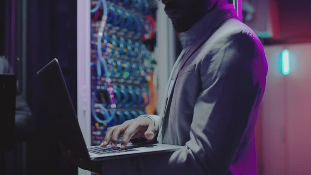 Cropped shot of African American data center engineer using laptop while working in server room