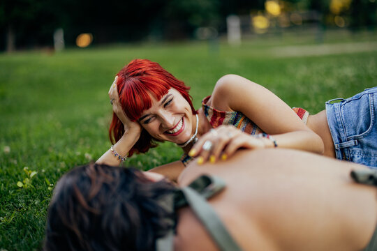 Smiling girl talking to her girlfriend, enoying laying on the grass, outdoor.