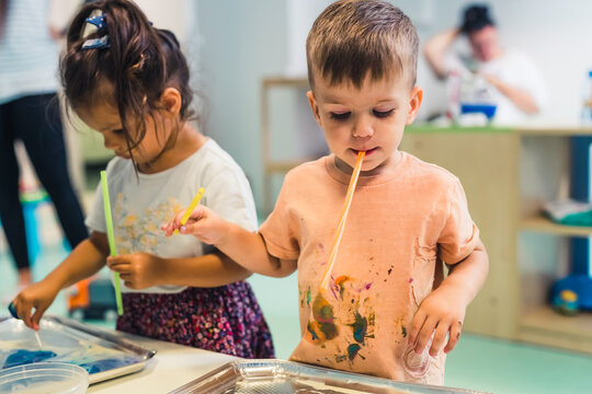 Multi-cultural Nursery School. Toddlers Playing With Striped Straws And Milk Painting, Using Nontoxic Food Coloring For Colors. Creative Kids Activity To Increase Concentration And To Develop Fine