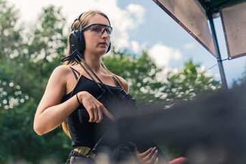 Caucasian woman wearing safety headphones and goggles looking at camera holding submachine gun. Outdoor shooting range. Horizontal shot. High quality photo