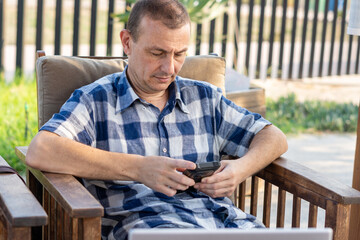 Relaxed sitting man using phone outdoors. 