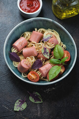 Green bowl with threaded spaghetti hot dog bites on a dark-brown stone background, elevated view, vertical shot