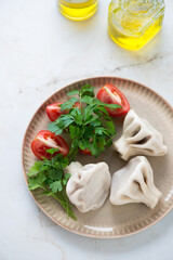 Georgian khinkali dumplings with fresh parsley and red tomatoes, elevated view on a light-beige marble background, vertical shot