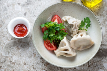 Plate with georgian meat dumplings khinkali, fresh parsley, tomato wedges and dip, horizontal shot on a light-brown granite background